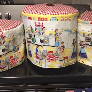 May include: Three red and white checkered stovetop covers with a vintage kitchen scene featuring women cooking and baking. The covers are made of fabric and have a red and white checkered pattern.