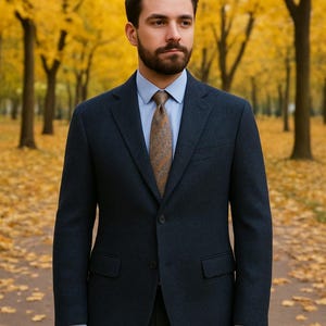 May include: A dark navy blue blazer with a notched lapel, two front buttons, and two flap pockets. The blazer is worn over a light blue collared dress shirt and a brown patterned necktie. The garment features long sleeves and a structured fit.