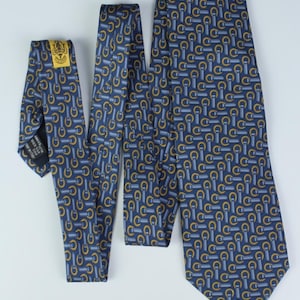 May include: A navy blue silk tie with a repeating pattern of gold and light blue equestrian-themed motifs. The tie is displayed in three sections, showcasing the design and the label.