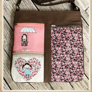 May include: A brown canvas crossbody bag with a zippered pocket and a flap closure. The bag has a patterned fabric lining with a pink and white floral design. The bag has a long adjustable strap and the text "Sami" is printed on the front of the bag.