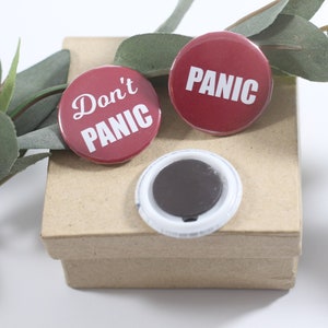 May include: Two red round buttons with white text. One button says "Don't Panic" and the other says "PANIC". The buttons are on a brown cardboard box.