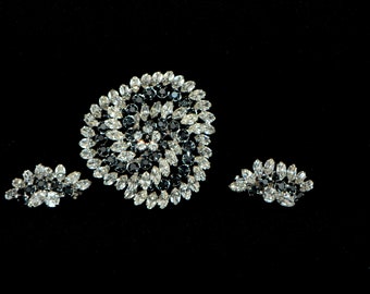 May include: A set of three black and white rhinestone brooches. The largest brooch is a circular design with a swirl pattern. The two smaller brooches are crescent shaped.
