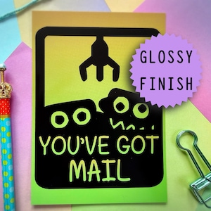 Può includere: Biglietto di auguri con finitura lucida, con una grafica di una macchina a pinza con due mostri dei cartoni animati e la scritta "YOU'VE GOT MAIL". Un adesivo a forma di stella viola recita "GLOSSY FINISH".