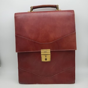 May include: A burgundy leather briefcase with a brass handle and lock. The briefcase has a flap closure and a textured leather exterior.