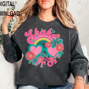 May include: A black sweatshirt with a retro-style graphic design featuring the text "Shake It Off" in pink and green lettering, a rainbow, heart-shaped sunglasses, and floral accents.