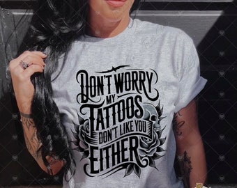 May include: A gray t-shirt with a black graphic that says "Don't Worry My Tattoos Don't Like You Either". The graphic includes a skull and rose.