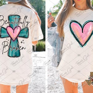 May include: White t-shirt with a teal blue cross and a pink heart in the center. The text "Beautifully Broken" is written below the cross.