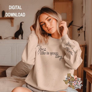 Puede incluir: Una sudadera beige con el texto "Your life is your story" y "Write it well. Edit often." en la parte delantera. La sudadera tiene un diseño floral con un contorno de Texas en la manga.