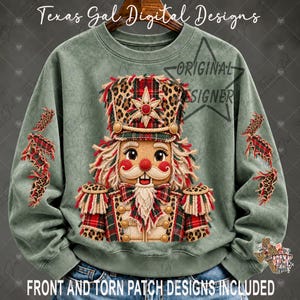May include: A sage green crewneck sweatshirt featuring a central graphic of a nutcracker with a leopard print hat and uniform accents. The design includes red and green plaid details, frayed edges, and the text Texas Gal Digital Designs.