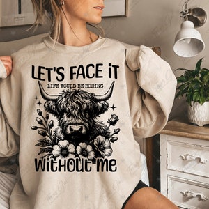 May include: A beige sweatshirt with a black graphic of a Highland cow with flowers and the text "Let's face it, life would be boring without me."