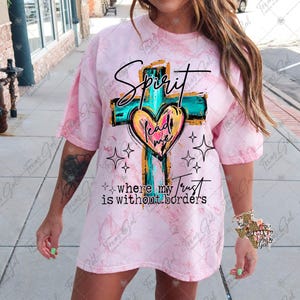 Op de afbeelding: Een roze tie-dye T-shirt met een afbeelding van een kruis en een hart met de tekst "Spirit lead me where my trust is without borders".