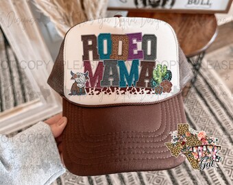 May include: Brown and white trucker hat with a white mesh back. The front of the hat has a colorful graphic that says "Rodeo Mama" with a cow and cactus design. The hat also has a small Texas-shaped patch with the words "Texas Gal" on it.