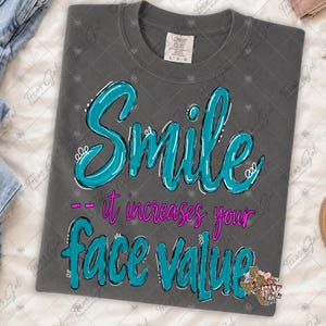 Może przedstawiać: Ciemnoszary t-shirt z okrągłym dekoltem z napisem "Smile it increases your face value" wykonanym pogrubioną turkusową kursywą oraz jaskraworóżowymi literami bezszeryfowymi. Projekt zawiera białe obrysy i akcenty na turkusowym tekście.