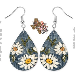 Op de afbeelding: Een paar denim-ge&iuml;nspireerde oorhangers met witte madeliefjes-borduurwerk. De oorbellen zijn traanvormig en hebben zilveren haakjes.