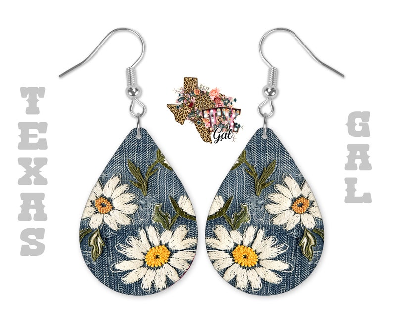 Op de afbeelding: Een paar denim-ge&iuml;nspireerde oorhangers met witte madeliefjes-borduurwerk. De oorbellen zijn traanvormig en hebben zilveren haakjes.