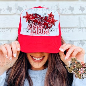 May include: Red and white trucker hat with a white mesh back. The hat has a white pom-pom and star design with the text "Cheer Mom" in red and white.