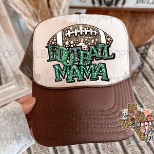 Könnte beinhalten: Eine braune und weiße Trucker-Kappe mit braunem Netzrücken. Die Vorderseite der Kappe zeigt einen weißen Football mit grünen und goldenen Strasssteinen und dem Text "Football Mama".