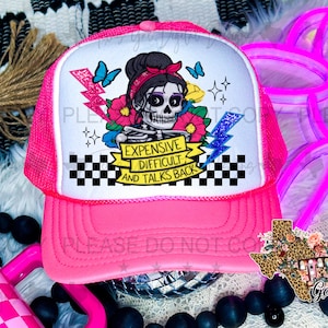 Op de afbeelding: Roze trucker-pet met een wit mesh-achterpaneel. De voorkant van de pet heeft een kleurrijke afbeelding van een skelet met een bloemenkroon en de tekst "Expensive, Difficult, and Talks Back".