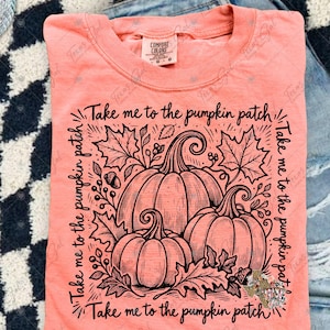 May include: A coral-colored t-shirt featuring a black line-art graphic of three pumpkins surrounded by autumn leaves and acorns. The text "Take me to the pumpkin patch" is printed in a square border around the central pumpkin illustration.