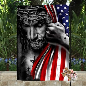 May include: A black and white image of Jesus with a crown of thorns, holding an American flag. The flag is red, white, and blue with stars. The image is a garden flag.