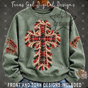 May include: A sage green crewneck sweatshirt featuring a central cross graphic with a red and black plaid pattern, surrounded by frayed fringe detailing. The sleeves display matching plaid patches with distressed edges.