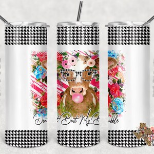 Peut inclure: Un gobelet en acier inoxydable blanc avec un motif pied-de-poule noir et blanc en haut et en bas. Le centre du gobelet présente un motif floral coloré avec une vache portant des lunettes et soufflant une bulle. Le texte "I Bust My Bubble" est imprimé sur le gobelet.