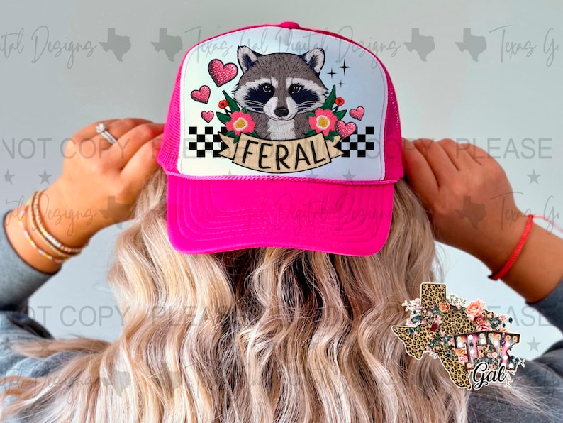 May include: Pink trucker hat with a black and white checkered pattern, a raccoon with hearts and flowers, and the word "Feral" in white lettering. The hat is worn by a person with long blonde hair.