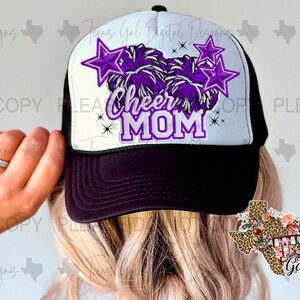 Puede incluir: Una gorra de camionero negra y blanca con un diseño de pompón morado y blanco y el texto "Cheer Mom".