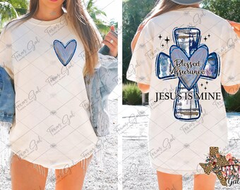 May include: White t-shirt with a blue and white cross design. The cross has a heart in the center with the text "Blessed Assurance" and the words "Jesus is Mine" below the cross.