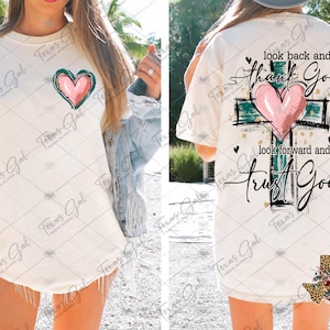 May include: White t-shirt with a green and pink heart and the text "look back and thank God, look forward and trust God" on the back. The shirt also has a small Texas-shaped design with a floral pattern on the bottom right.