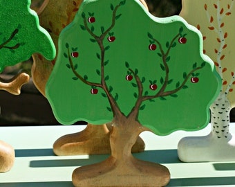 May include: A set of wooden toy trees, painted in green, brown, and yellow. The trees are decorated with red painted apples and leaves. The trees are standing on a green surface.