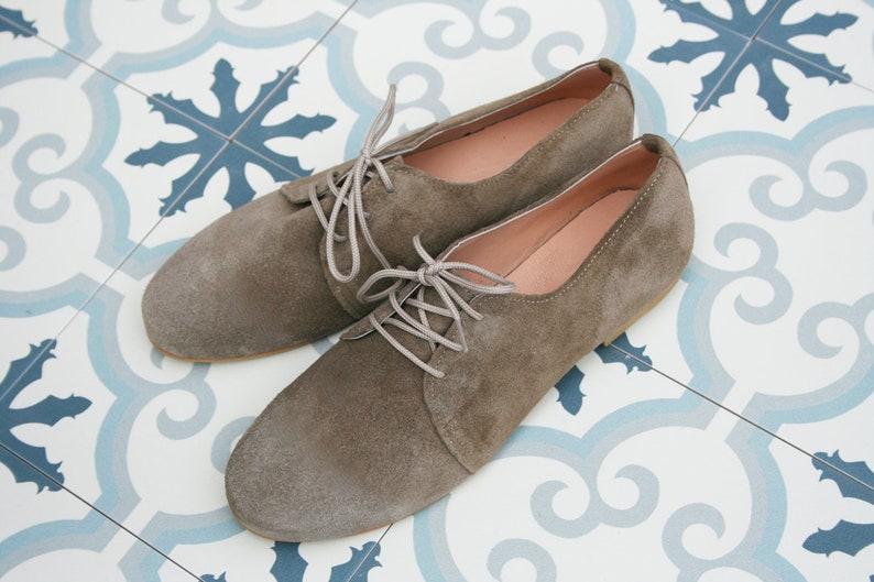May include: A pair of brown suede lace-up shoes with a rounded toe. The shoes are on a white and blue patterned tile floor.