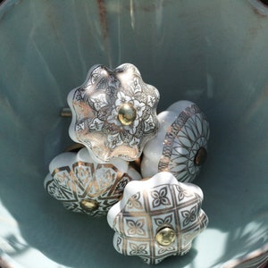 Pode incluir: Quatro botões de gaveta de cerâmica branca com detalhes dourados e padrões intrincados em uma tigela azul claro.