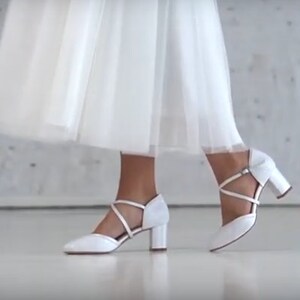 K&ouml;nnte beinhalten: Wei&szlig;e Brautschuhe mit einem Kreuzriemen-Design und einem Blockabsatz.