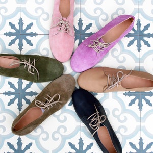 May include: Six pairs of suede lace-up shoes in different colors, including pink, purple, green, brown, beige, and blue, arranged in a star shape on a white and blue tiled floor.