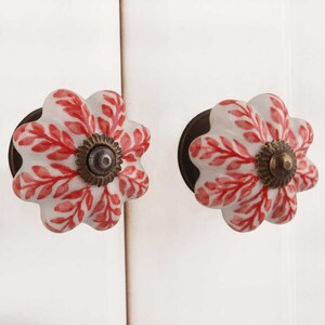 K&ouml;nnte beinhalten: Zwei wei&szlig;e Keramik-Schrankkn&ouml;pfe mit rotem Blumendesign und einem Messingkern.