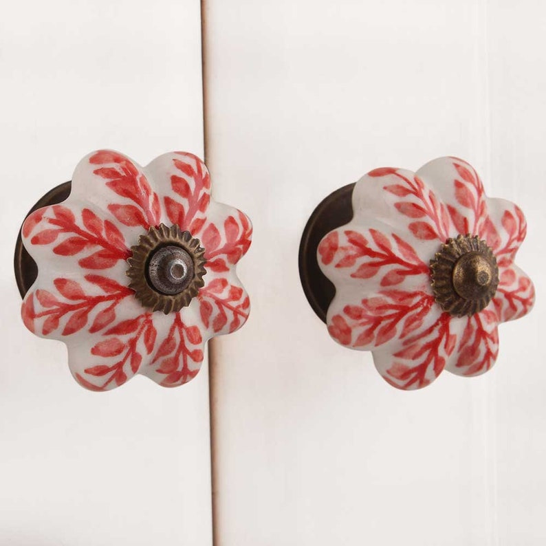 K&ouml;nnte beinhalten: Zwei wei&szlig;e Keramik-Schrankkn&ouml;pfe mit rotem Blumendesign und einem Messingkern.