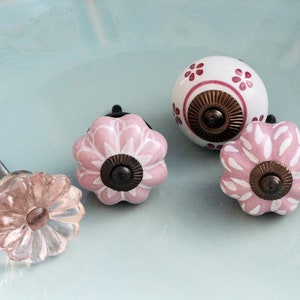 Puede incluir: Cuatro pomos de caj&oacute;n de cer&aacute;mica con dise&ntilde;os florales. Dos pomos son blancos con detalles florales rosas, uno es rosa con detalles florales blancos y uno es rosa claro con un dise&ntilde;o floral.