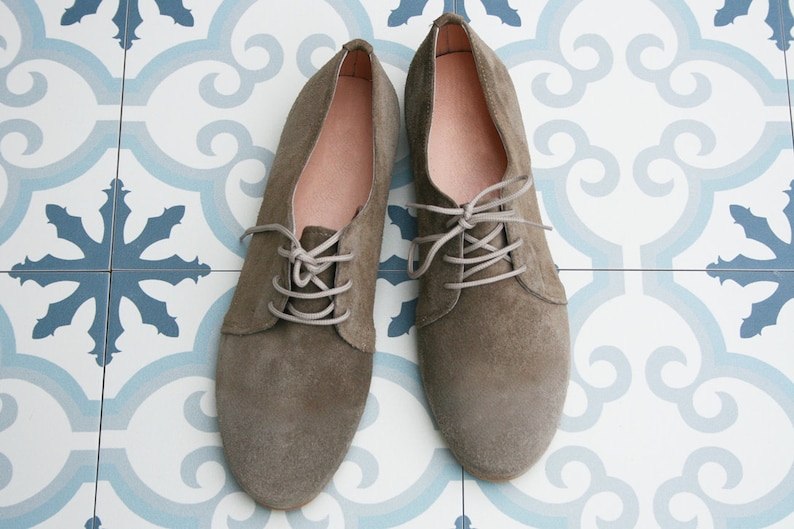 May include: A pair of gray suede lace-up shoes with light gray laces. The shoes are on a white and blue patterned tile floor.