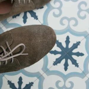 May include: A pair of brown suede lace-up shoes with white laces. The shoes are on a white and blue tiled floor.