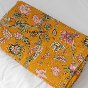 May include: A mustard yellow kantha quilt with a floral pattern. The quilt is made of cotton and has a hand-stitched design. The quilt is folded in half and is lying on a white surface. The text "Handloom Palace Art" is visible in the image.