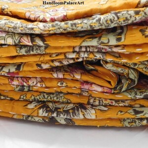 May include: A stack of yellow kantha quilts with floral patterns. The quilts are folded and layered, showing the intricate stitching and colorful designs.