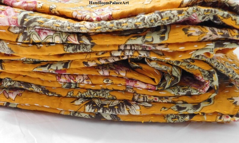 May include: A stack of yellow kantha quilts with floral patterns. The quilts are folded and layered, showing the intricate stitching and colorful designs.