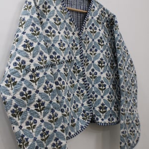 Könnte beinhalten: Eine gesteppte Jacke mit blauem und weißem Blumenmuster, V-Ausschnitt und langen Ärmeln. Die Jacke hat ein handloompalaceart Logo auf der Vorderseite.