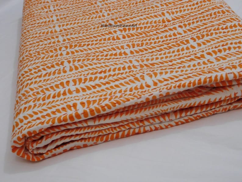 K&ouml;nnte beinhalten: Orange-wei&szlig;e Baumwoll-Kantha-Steppdecke mit einem Blatt-Muster. Die Decke ist dreifach gefaltet und der Stoff ist strukturiert.