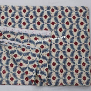 Puede incluir: Una colcha kantha doblada con fondo blanco y un patr&oacute;n repetitivo de hojas azules y flores rojas. La colcha est&aacute; hecha de algod&oacute;n y est&aacute; cosida a mano. El texto "HandloomPalaceArt" es visible en la colcha.