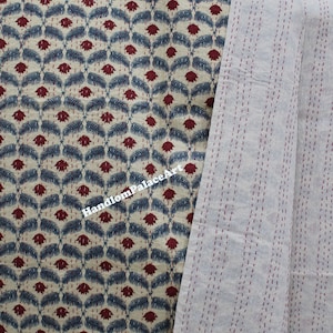 Puede incluir: Una colcha kantha de color crema con un patr&oacute;n repetitivo de flores rojas y hojas azules. La colcha est&aacute; cosida a mano con hilo rojo y tiene un reverso liso de color crema.