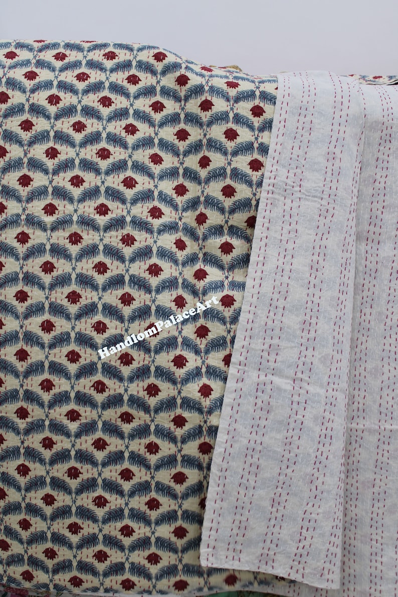 Puede incluir: Una colcha kantha de color crema con un patr&oacute;n repetitivo de flores rojas y hojas azules. La colcha est&aacute; cosida a mano con hilo rojo y tiene un reverso liso de color crema.