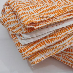 K&ouml;nnte beinhalten: Eine wei&szlig;e und orangefarbene Kantha-Steppdecke mit einem sich wiederholenden Muster aus orangefarbenen Bl&auml;ttern. Die Steppdecke ist dreifach gefaltet und der Stoff ist weich und strukturiert.