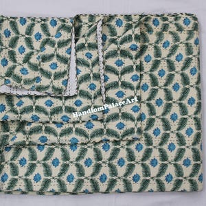 Peut inclure: Une courtepointe kantha blanche avec un motif floral vert et bleu. La courtepointe est pliée en deux et porte une étiquette Handloom Palace Art.